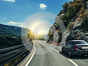 Black car rushing along a high-speed highway in the sun.