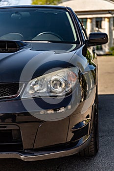 Black car in static on a sunny day. Front view half of the car -hood, headlight and a wheel. Vertical orientation.