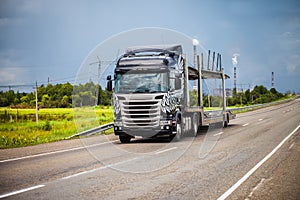 Black car transporter on a road with power station on the background