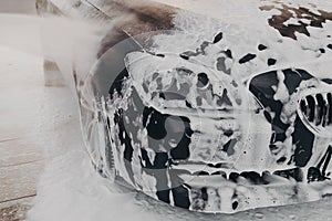 Black car in white snow foam during carwashing and cleaning outdoors