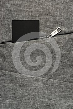 Black card peeks out from zipper pocket of gray textured fabric background
