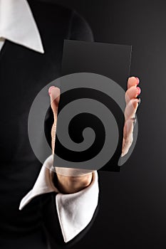 Black cardboard card in a woman`s hand with a beautiful manicure and white cuffs and collar on a black background.