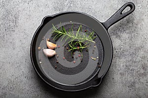 Black cast iron frying pan with rosemary, garlic, pepper top view