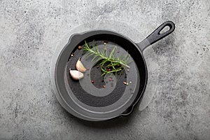Black cast iron frying pan with rosemary, garlic, pepper top view