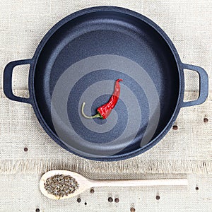 Black cast-iron frying pan, wooden spoon, red hot peppers and sp