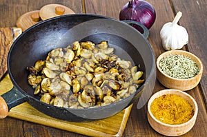 Black cast iron pan with fried mushroom slices on wooden background.