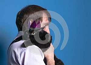 Cat in pink shiny crown sitting on man sholder with extended paws on blue background photo