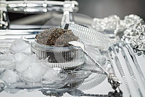 Black caviar. Black sturgeon caviar in a cut-glass bowl and a metal spoon on a silver tray filled with ice