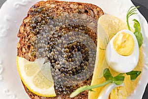 Black caviar on a sandwich with eggs, lemon, greenery