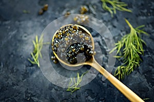 Black caviar in a spoon on dark background. Natural sturgeon black caviar closeup. Delicatessen. Top view photo