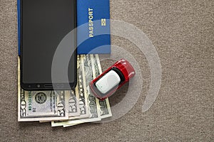 Black cellphone, money American dollars banknotes bills, passport and toy car on copy space background, top view. Travel light,