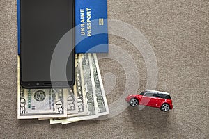 Black cellphone, money American dollars banknotes bills, passport and toy car on copy space background, top view. Travel light,