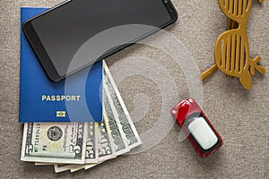 Black cellphone, money American dollars banknotes bills, passport, toy car and funny sunglasses on copy space background, top view