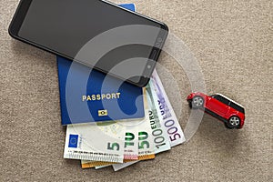 Black cellphone, money euro banknotes bills, passport and toy car on copy space background. Travel light, comfortable journey