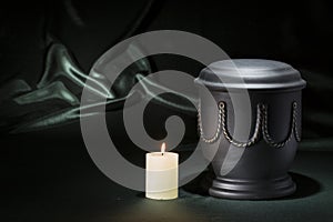 Black cemetery urn with burning candle on deep green background