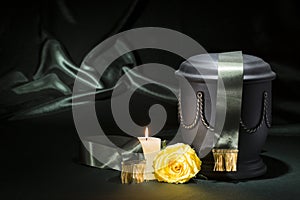 Black cemetery urn with burning candle deep green ribbon, and yellow rose on dark green background