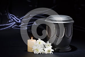 Black cemetery urn with burning candle white chrysanthemum on deep blue background