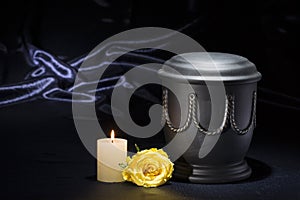 Black cemetery urn with burning candle yellow rose on deep blue background