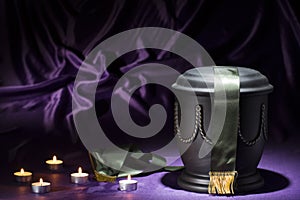 Black cemetery urn with candles, and deep green ribbon on dark purple background