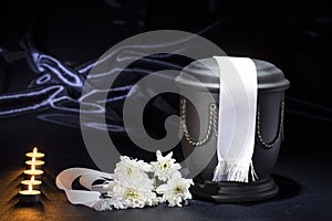 Black cemetery urn with candles and white chrysanthemum, and white ribbon