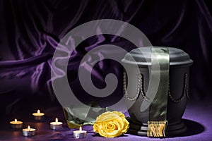 Black cemetery urn with candles yellow rose, and dark green ribbon, on deep purple background