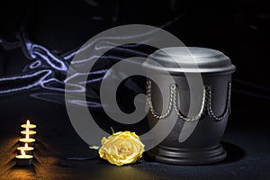 Black cemetery urn with candles yellow rose on deep blue background