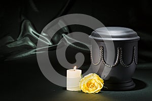 Black cemetery urn with churning candle yellow rose on dark green background