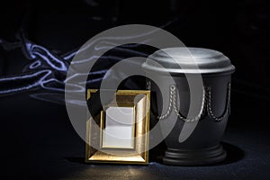 Black cemetery urn with golden mourning frame on dark blue background