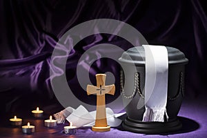 Black cemetery urnk with cross and candles and white ribbon on deep purple background