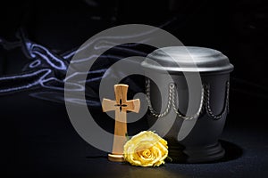 Black cemetery urnk with wooden cross, yellow rose on deep blue background