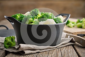 Black ceramic saucepan with cooked broccoli and cauliflower on kitchen table