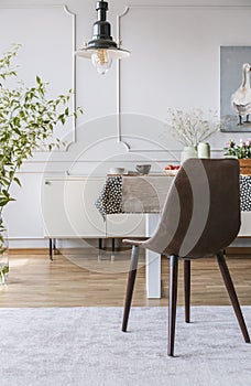 Black chair on grey carpet at table in dining room interior with lamp and wall with molding. Real photo