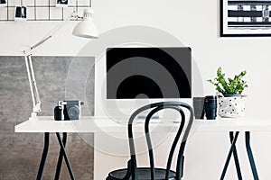 Black chair by a white desk with a computer and a lamp in a modern home office interior for a professional photographer freelancer