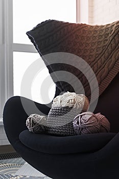 black chair with wool ball of yarn and knitting needles in the armrest