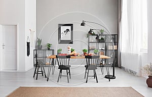 Black chairs at dining table with food in apartment interior with lamp and poster on grey wall