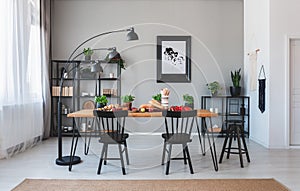 Black chairs and lamp at wooden table with food in grey dining room interior with poster