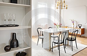 Black chairs at table with flowers under gold lamp in white modern dining room interior. Real photo