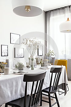 Black chairs at table with tableware in bright dining room interior