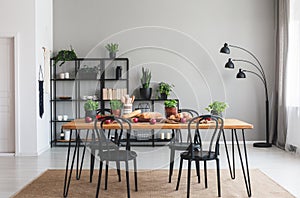 Black chairs and wooden table with food on brown carpet in grey dining room interior