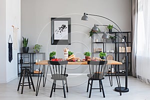 Black chairs at wooden table with food in grey dining room interior with poster and lamp