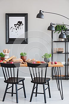 Black chairs at wooden table with food in grey dining room interior with poster and lamp