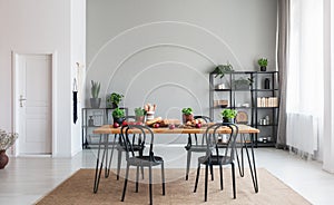 Black chairs at wooden table with food in grey dining room interior with white door. Real photo