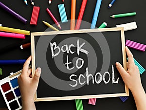 black chalk board with handwritten Back to school in children& x27;s hands and school felt-tip pens, paints, pen