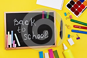 Black chalk board with handwritten Back to school and school supplies chalk, felt-tip pens, paints, pen, paper clips, plasticine,