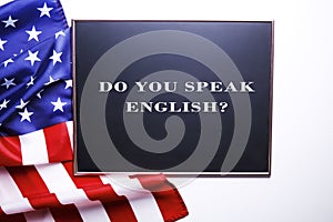 Black chalkboard with the question do you speak English? written in it and the flag of the United States of America.