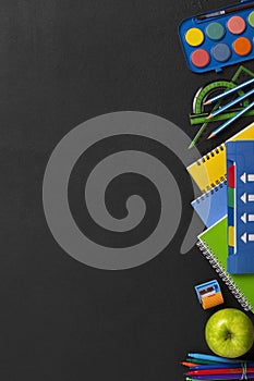 Black chalkboard school background with school supplies and stationery items, empty copy space for text