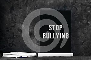 Black chalkboard white text Stop Bullying on dark background with notebook and pen. School education board with sign