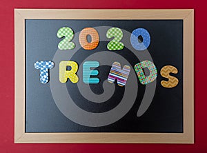 Black chalkboard with wooden frame, text 2020 trends in colorful numbers, red wall background