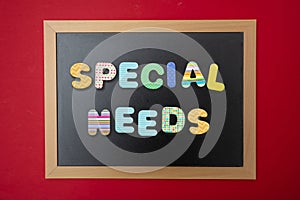 Black chalkboard with wooden frame, text special needs in colorful letters, red wall background photo