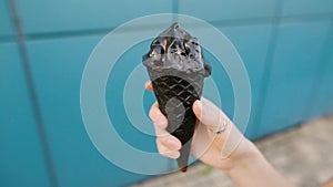 Black charcoal ice cream in a female hand on a blue background.